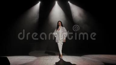 一个女人在黑暗中在白色聚光灯下上台的肖像。